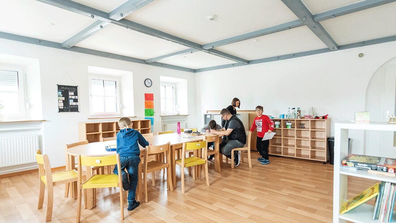 Gruppenraum einer heilpädagogischen Tagesstätte mit Kindern und Fachkräften am Tisch