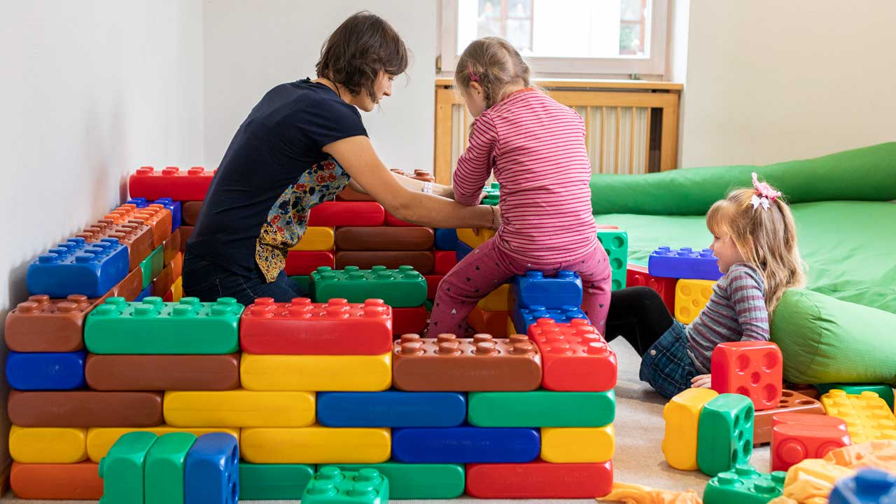 Fachkraft und Kinder bauen mit bunten Bausteinen auf dem Boden