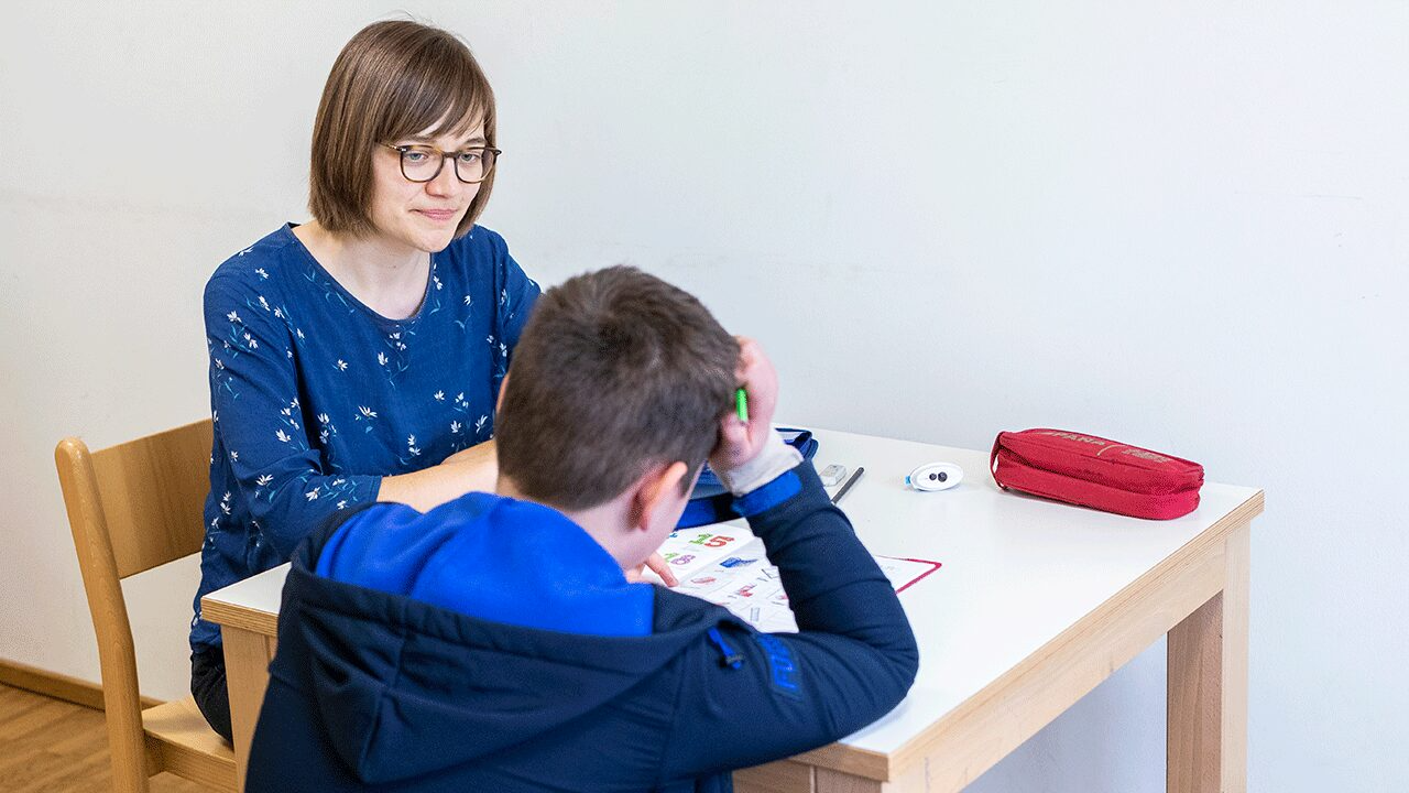 Fachkraft hilft einem Kind bei den Hausaufgaben