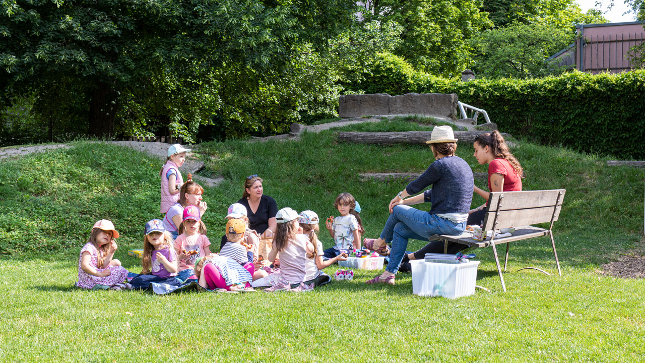 Gruppe von Kindern und Erwachsenen im Gespräch im Grünen